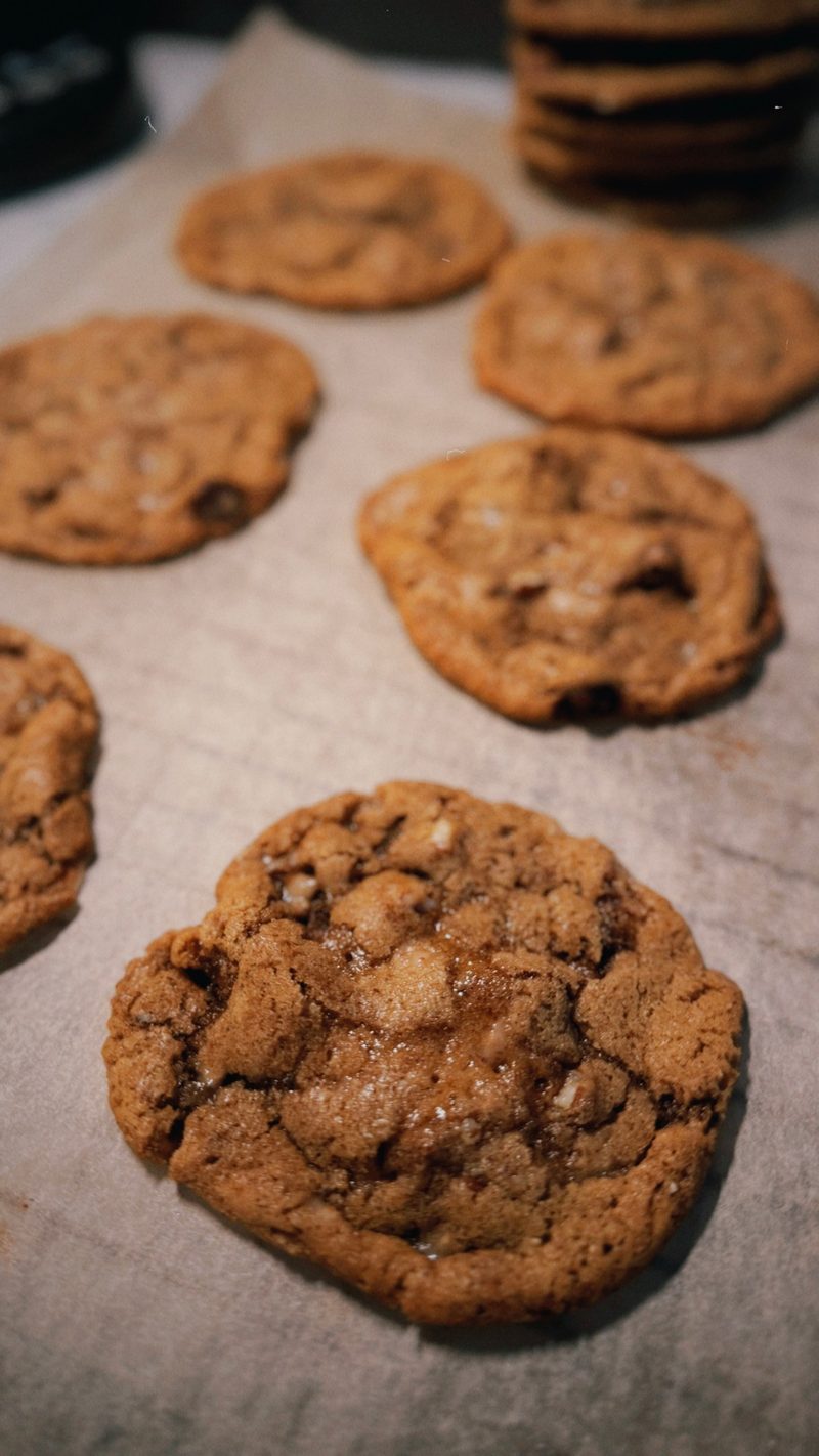 Freshly baked chocolate chip cookies with gooey centres cooling on parchment paper