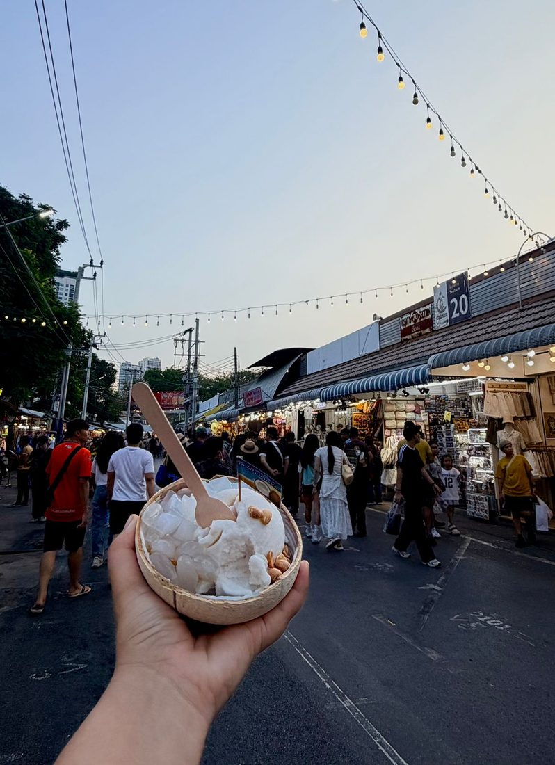 Coconut ice cream served in a coconut shell with peanuts, held up at a night market