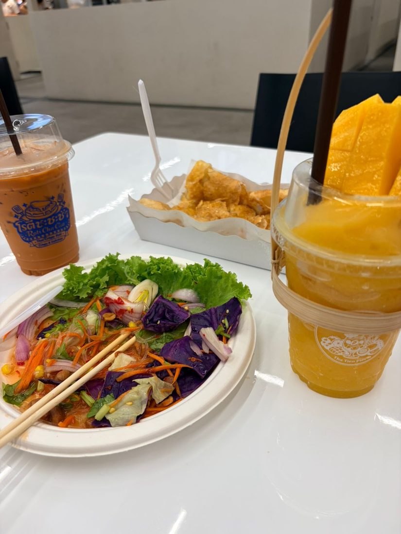 A vibrant Thai salad with purple cabbage and carrots, next to a Thai iced tea and crispy snacks at a market