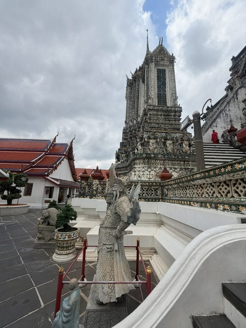 An ornate guardian statue in front of the tiered spire of Wat Arun temple in Bangkok