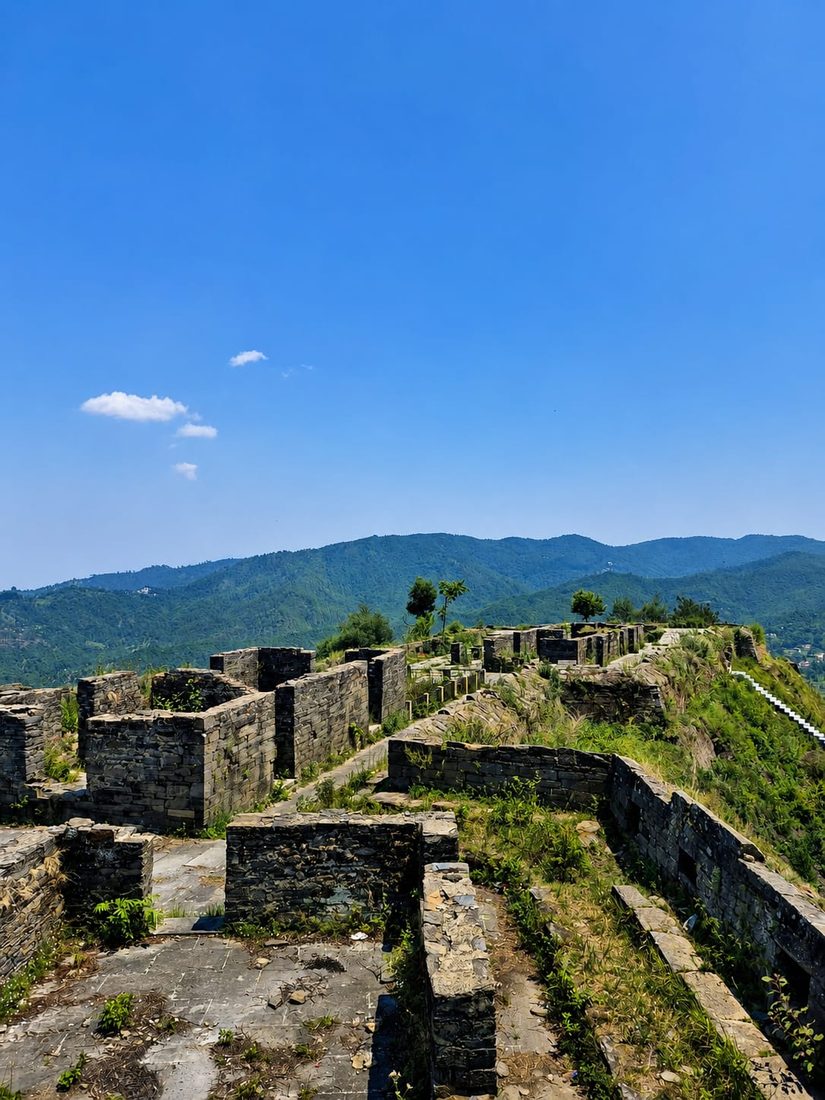 Weathered stone fort ruins along a hilltop ridge under a clear blue sky, mountains in the background